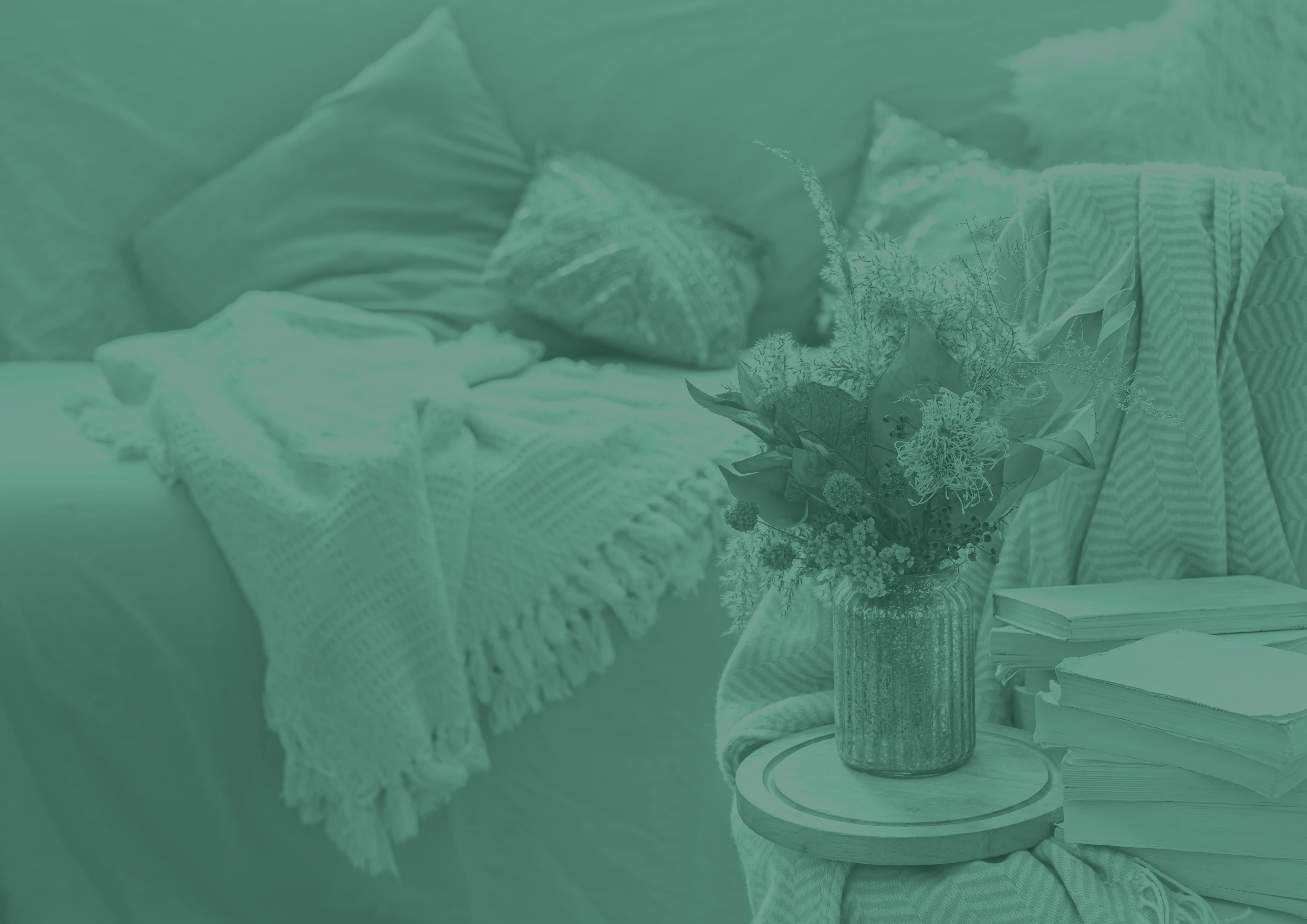A styled bedroom with a vase of dried flowers and books